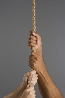 Close up of four hands hanging on rope