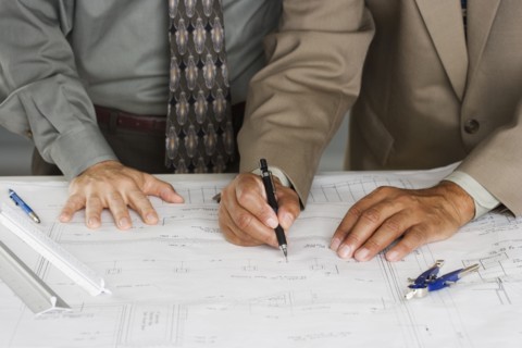 Mid section view of businessmen drawing building plans