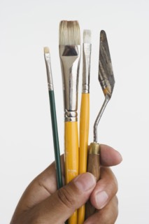 Close up of hands holding paintbrushes and palette knife