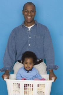 Father doing laundry with baby daughter in hamper