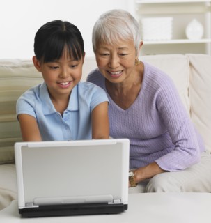 Asian grandmother and granddaughter using laptop on sofa