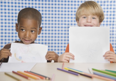 Two young boys holding up drawings