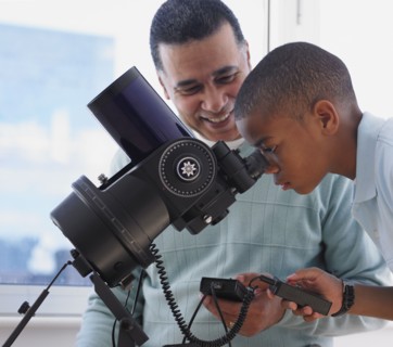 African boy looking into microscope with father