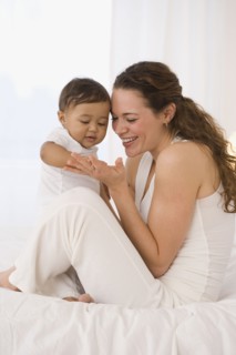 Hispanic mother playing with baby on bed
