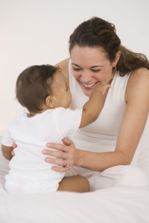 Hispanic mother playing with baby on bed