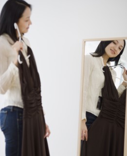 Asian woman holding dress up in front of mirror