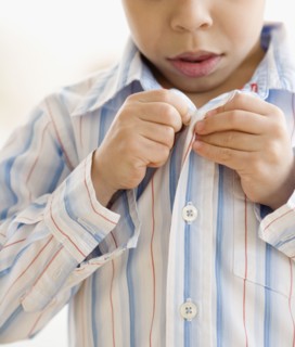 Hispanic boy buttoning shirt