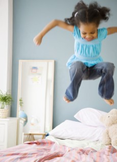 Mixed race girl jumping on bed