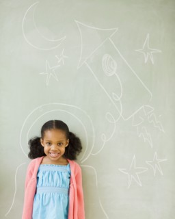 Mixed race girl standing by drawings on blackboard