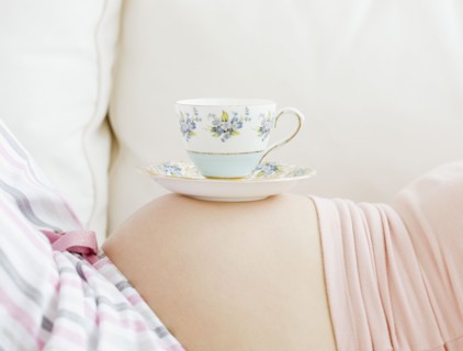 Pregnant Asian woman balancing tea cup on stomach