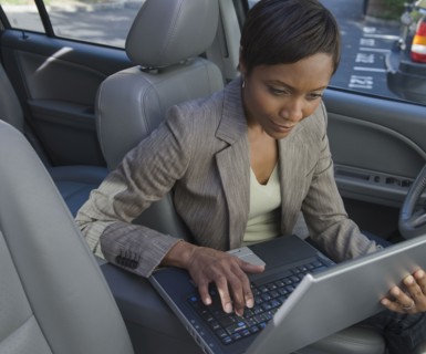 African businesswoman typing on laptop in car