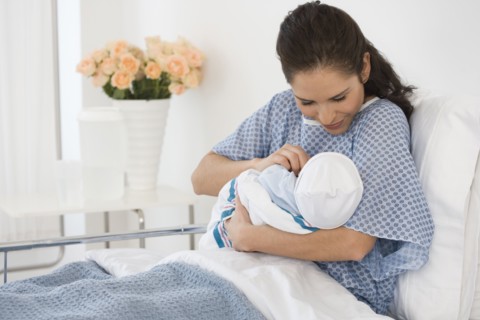 Hispanic mother holding newborn baby in hospital bed