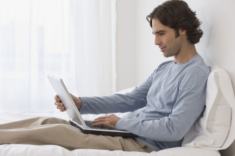 Hispanic man using laptop on bed