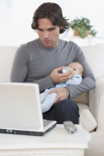 Hispanic father feeding baby and looking at laptop