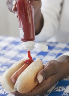 African woman putting ketchup on hot dog