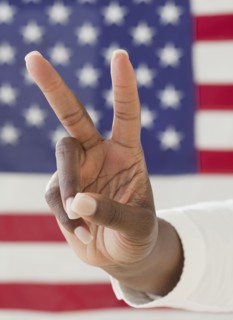 African woman making peace symbol near American flag