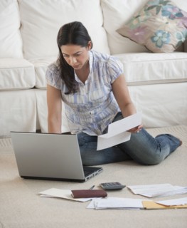 Hispanic woman paying bills with laptop on living room floor