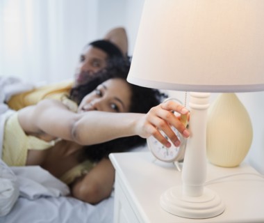 Woman in bed reaching to turn off bedside lamp