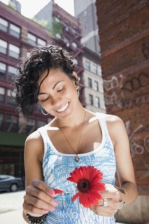 Mixed race woman picking petals off flower on urban street