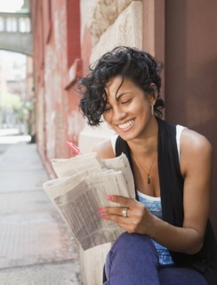 Mixed race woman reading classified ads on urban street