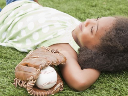 Mixed race girl laying next to baseball glove and ball