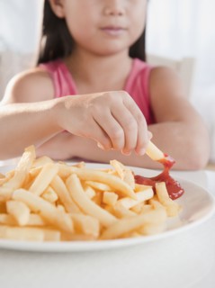 Mixed race girl eating French fries and ketchup
