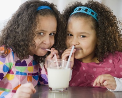 Hispanic sisters sharing glass of milk