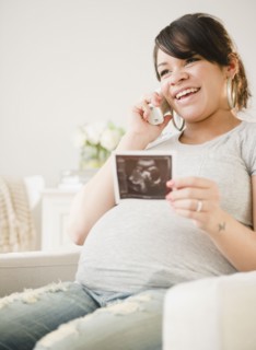 Pregnant Hispanic woman with sonogram picture talking on phone