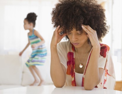 Mother with headache and daughter jumping on sofa