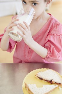 Mixed race girl drinking milk and eating sandwich