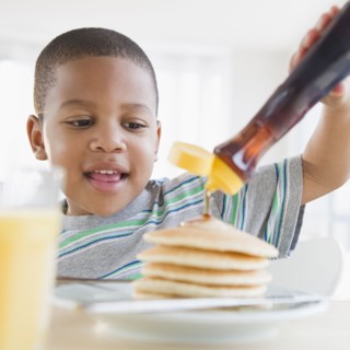 African American boy pouring syrup on pancakes
