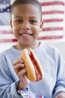 African American boy eating hot dog in front of American flag