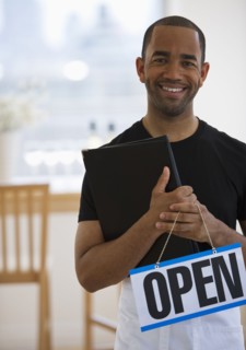 Mixed race waiter in restaurant holding menu and open sign