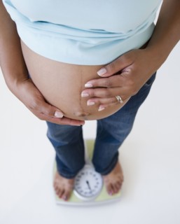 Pregnant Black woman holding stomach and standing on scale