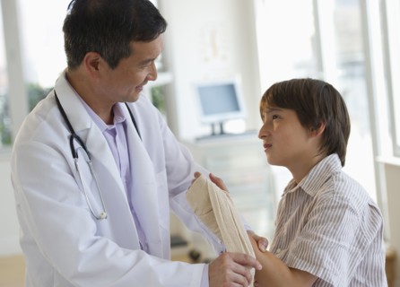 Doctor wrapping boy's hand with bandage in examination room