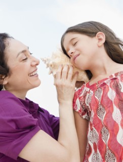 Mother holding seashell to daughter's ear
