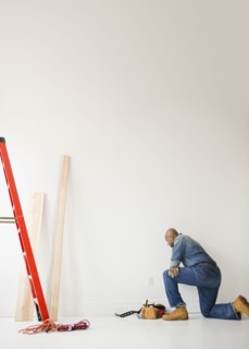 African American construction worker kneeling to look at wall
