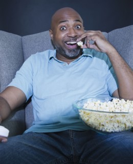 African American man eating popcorn and watching television