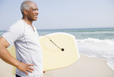 Black man holding body board on beach