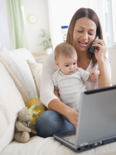 Mother holding baby and using telephone and laptop