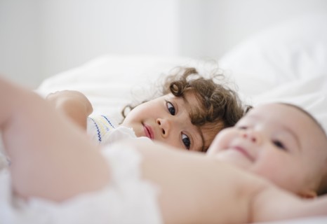 Mixed race girl watching baby sister on bed