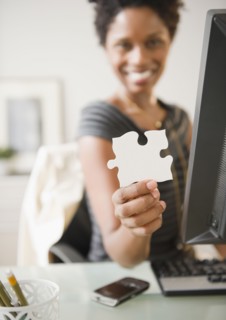 Black businesswoman holding puzzle piece at desk