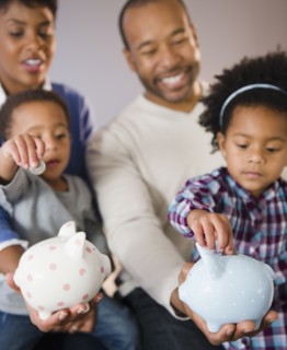 Black parents watching children put money in piggy bank