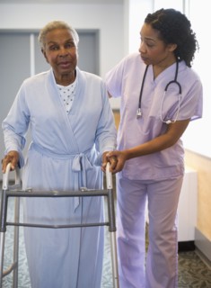 Nurse helping woman use walker in hospital hallway
