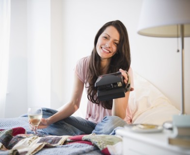 Brazilian woman sitting in bed with wine and instant camera