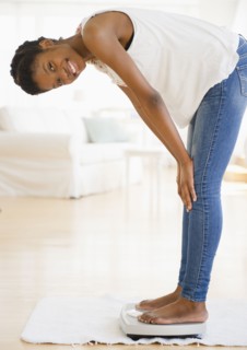 Smiling Black woman weighing herself