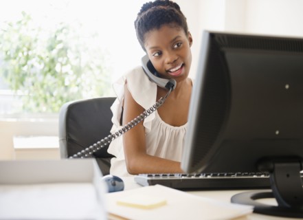 Black businesswoman talking on phone and using laptop