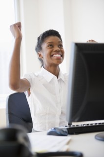 Excited Black businesswoman cheering at desk