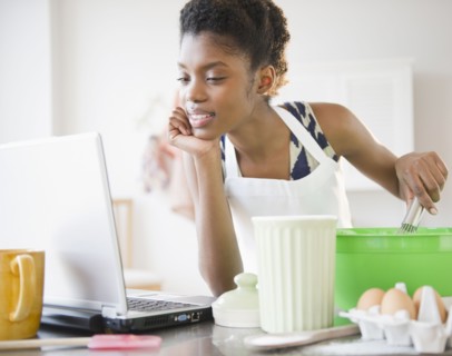 Black woman cooking and looking at recipe on laptop