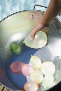 Hispanic girl picking water balloon out of bucket